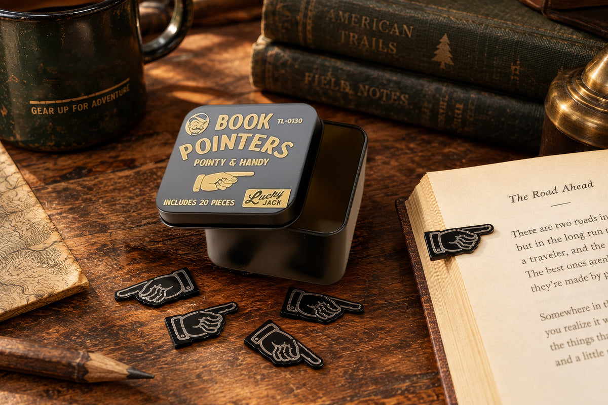 A tin of Book Pointers novelty book bookmarks displayed on a rustic wooden desk with an open book, pencil, mug, and books in the background.