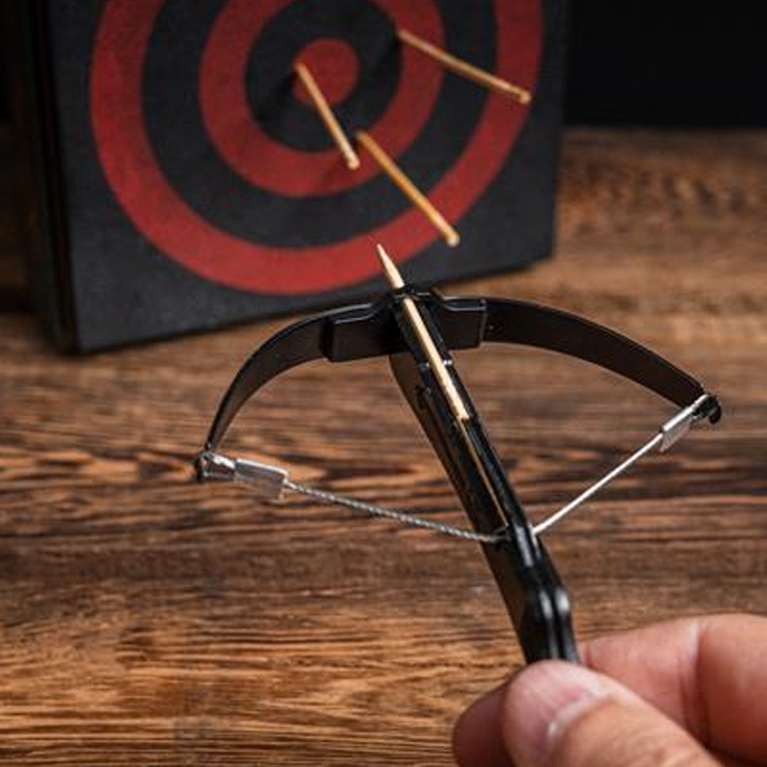 Hand holding a crossbow with an arrow aimed at a target on a wooden surface