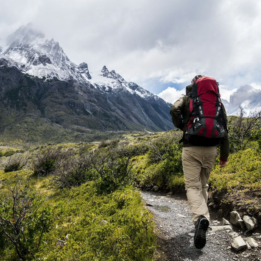 Man venturing forth on a trail towards a distant snow capped mountain
