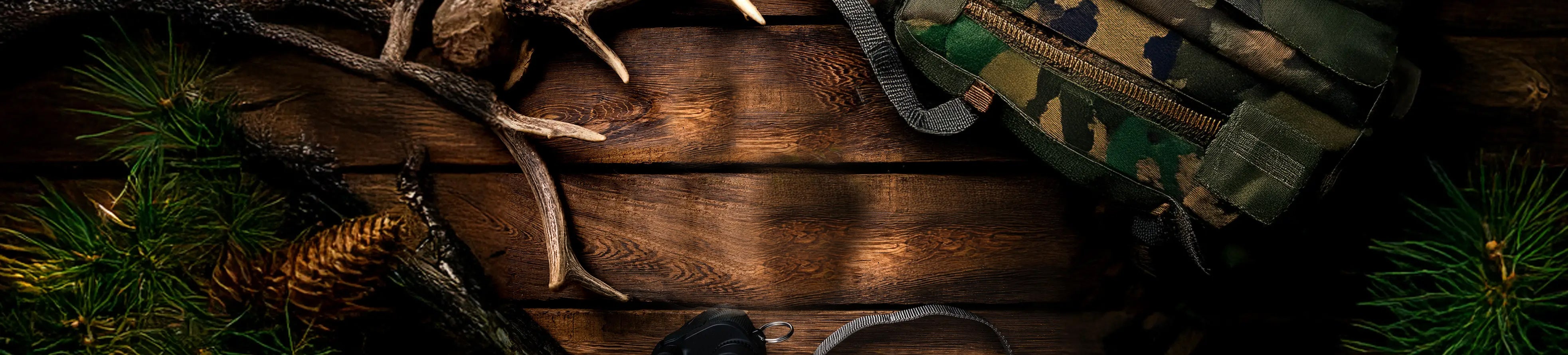 Wooden surface with hunting gear, including a rifle, camouflage bag, and deer antlers.