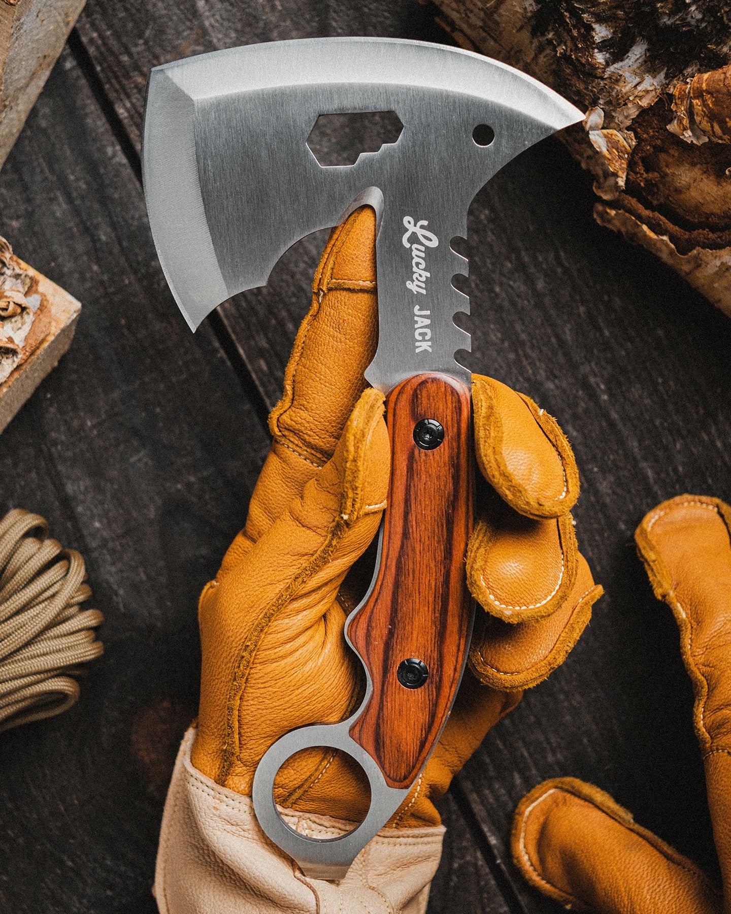 Hand holding a folding axe with leather glove on a wooden background