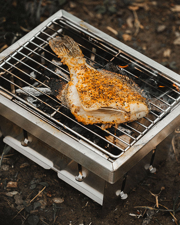 Fish being grilled on a small portable grill outdoors.