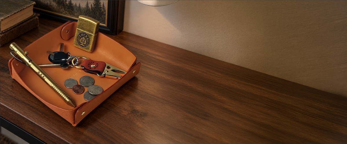 Leather valet tray on a wooden countertop displaying a pen, keychain, a lighter and spare change.